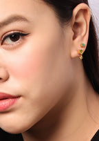Close-up of a woman's ear wearing a pair of small gold stud earrings with green and yellow-green stones.