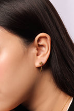 A close-up of a model's ear wearing a delicate gold dangle earring with a small floral cluster at the top.
