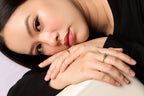 A close-up lifestyle shot of a woman resting her head on her hands, showcasing a delicate gold ring with a green stone on her index finger.