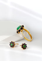 A gold ring and matching stud earrings set with green stones and dark blue accents, arranged on a clean white surface with soft shadows.