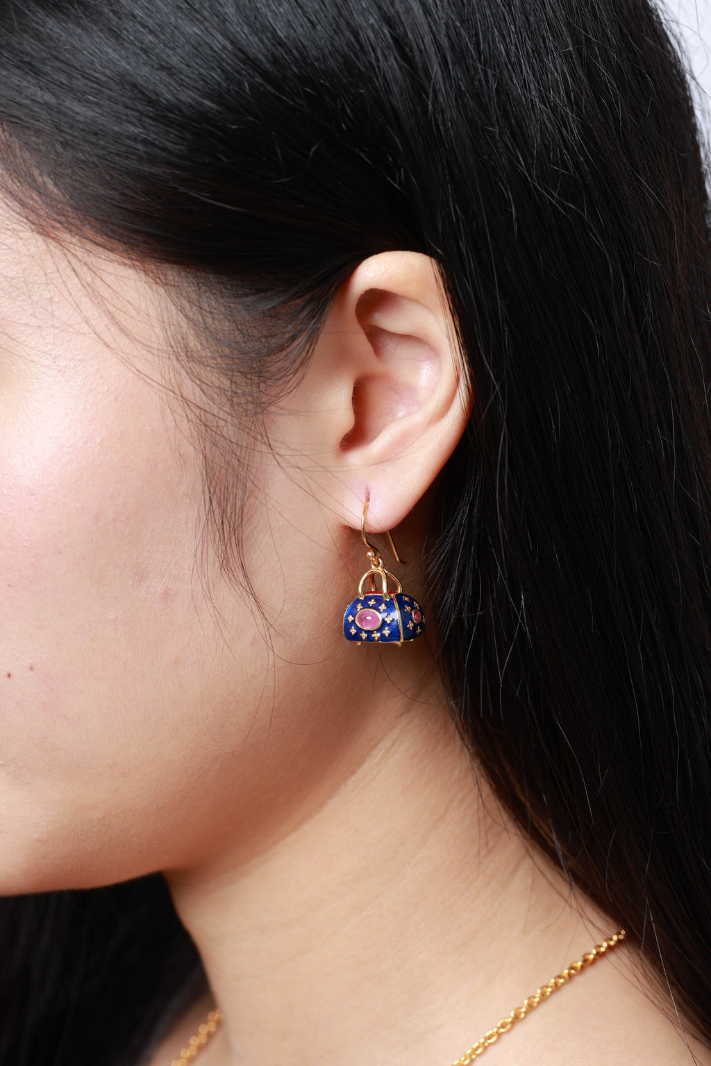 A close-up side profile of a woman wearing a dangling earring shaped like a small handbag. 