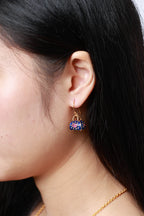 A close-up side profile of a woman wearing a dangling earring shaped like a small handbag. 