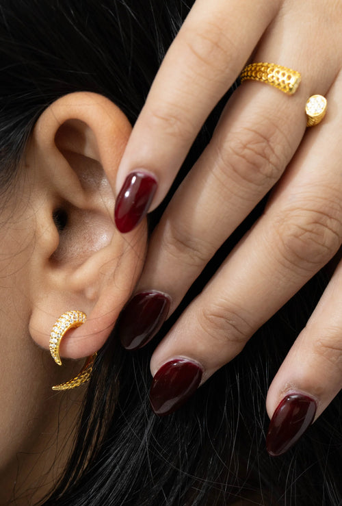 Gold hoop earring with clear stones and textured gold rings on hand with deep red nails