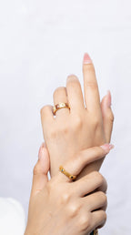 Two hands crossed together, showcasing two gold rings with small clear stones on the fingers against a clean white background.