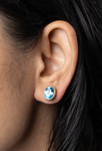 Oval blue topaz stud earring in gold setting on ear, elegant gemstone jewelry