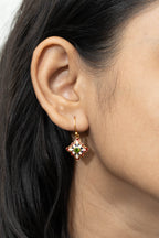 A close-up of a model's ear wearing a small gold-toned dangle earring with a floral star design and colorful enamel details.