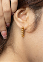 A close-up lifestyle shot of a model wearing a gold dangle earring and a matching gold beaded bracelet. 