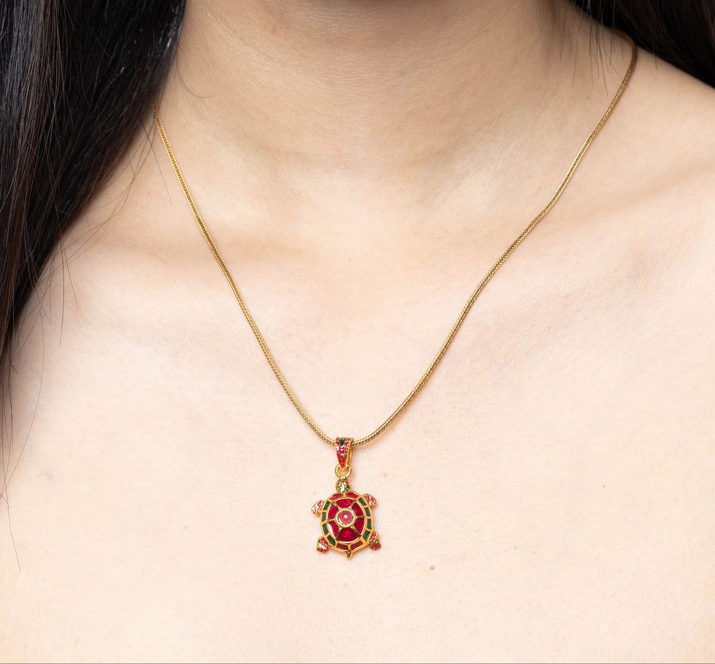 A close-up of a model wearing a delicate gold chain necklace with a small turtle pendant featuring a red center.