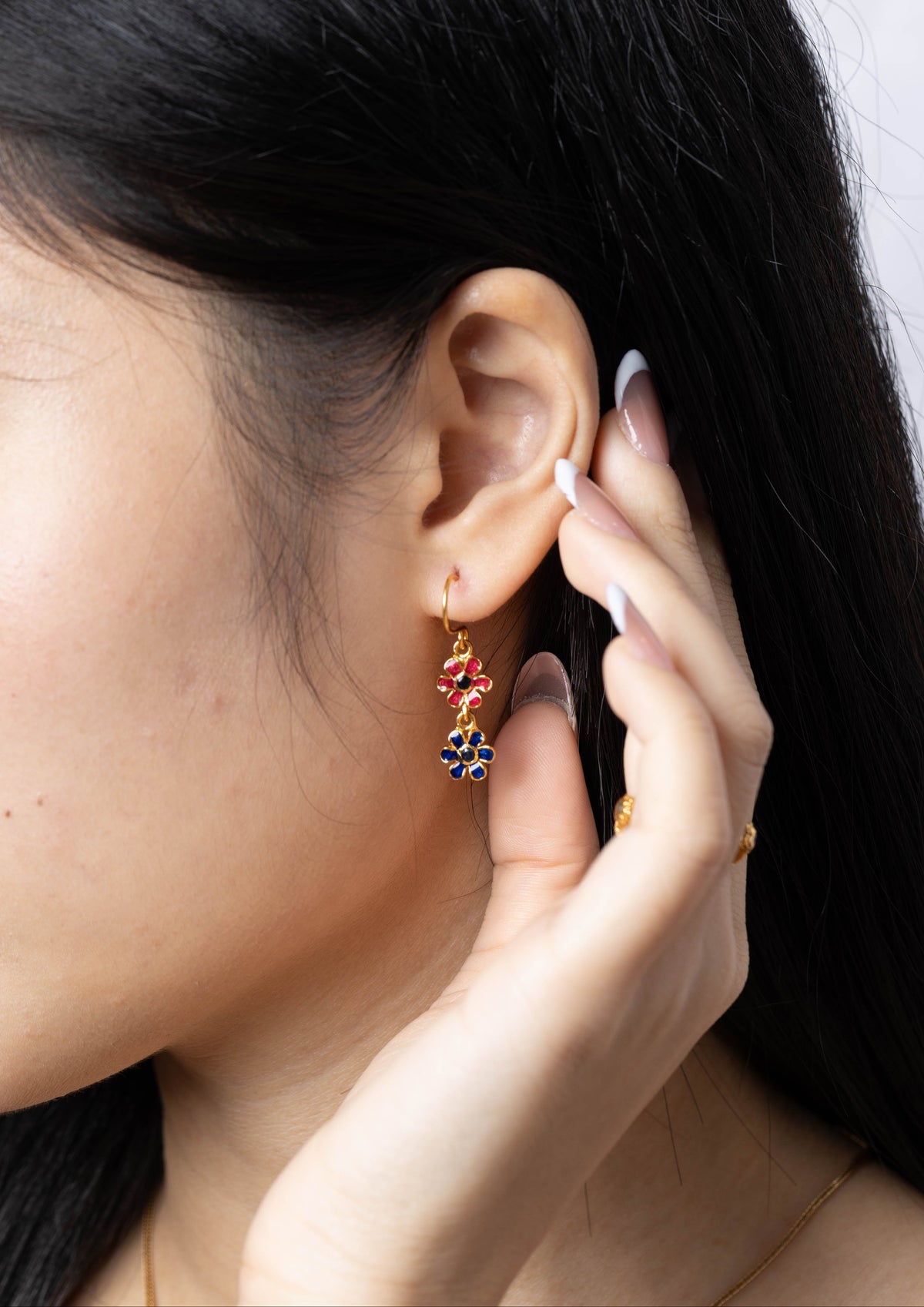 A close-up of a woman's ear wearing a gold dangle earring with colorful floral details, including red, blue, and yellow elements.