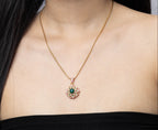 A close-up of a woman wearing a delicate gold chain necklace with a circular pendant featuring a green center and pink surrounding stones, paired with a black strapless top.