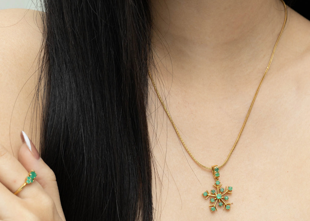 Gold snowflake pendant necklace with green gemstones, paired with matching ring, worn by woman with dark hair