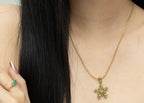 Gold snowflake pendant necklace with green gemstones, paired with matching ring, worn by woman with dark hair.