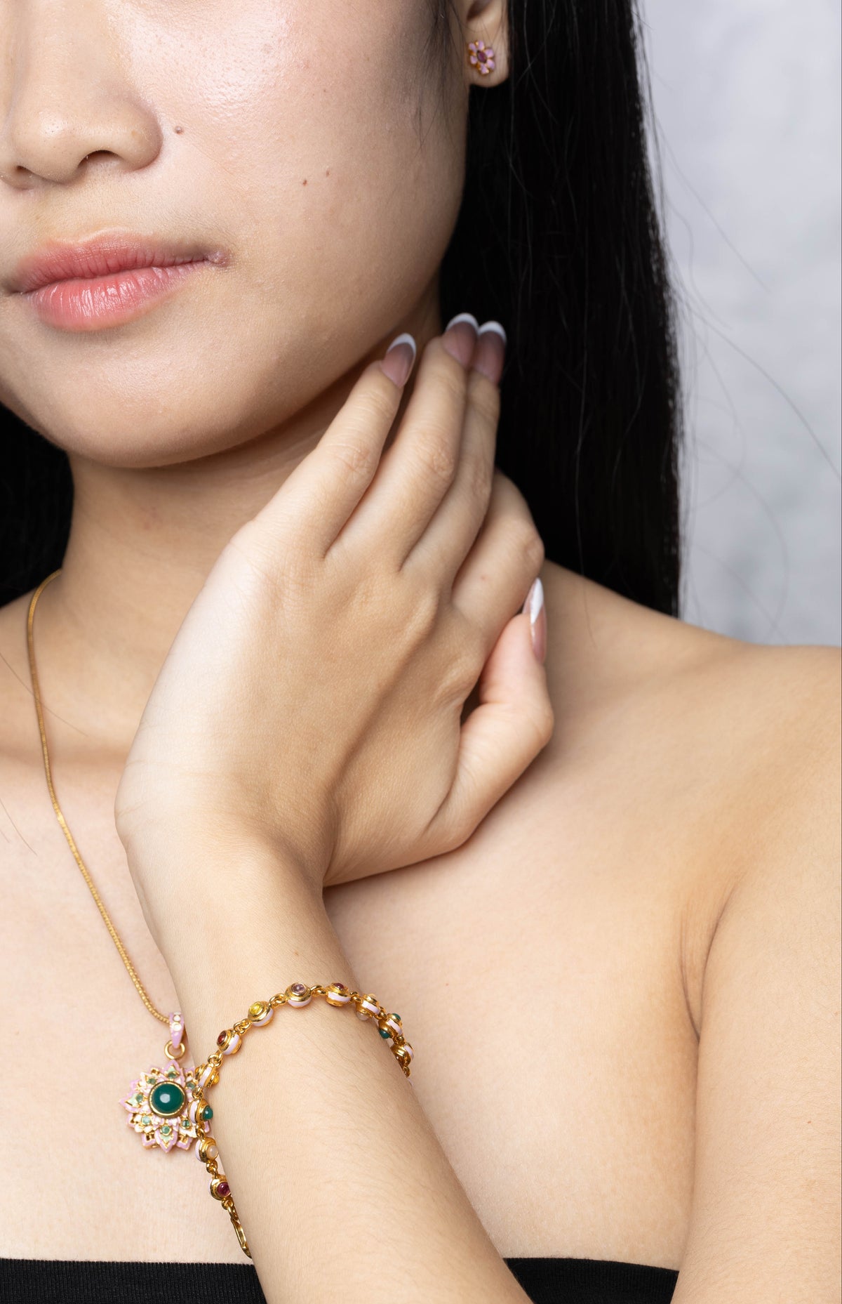 A close-up lifestyle shot of a woman wearing a delicate gold chain necklace and matching bracelet with a green and gold floral design.
