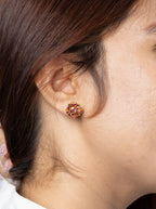 A close-up side profile of a woman wearing a small round stud earring with a warm amber-orange center and a gold-toned outer ring.
