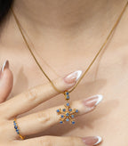 Gold snowflake pendant necklace with blue gemstones, paired with matching ring, worn on woman's hand