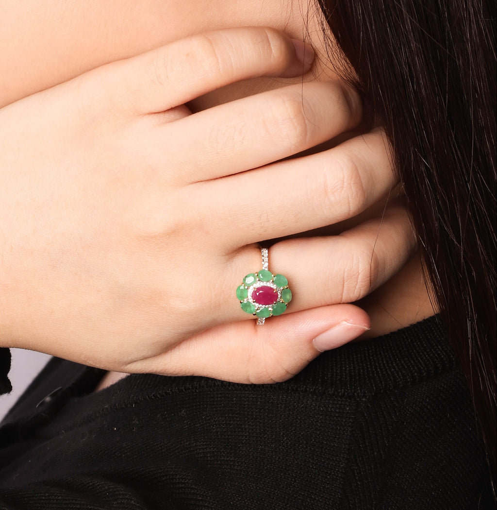 Close-up side profile of a woman wearing a small green and red stud earring and a matching green ring with a red center on her finger, against a light gray background.