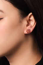 A close-up of a person's ear wearing a small flower-shaped stud earring with gold and pink metallic detailing.