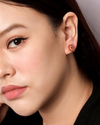 A close-up of a woman's ear wearing a small floral stud earring with red and gold petals.