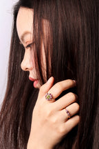 A close-up lifestyle shot of a woman with long dark brown hair, wearing two rings on her fingers.