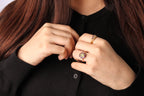 Close-up of a person wearing gold rings, including a prominent ring with a round pinkish gemstone and a smaller band ring, against a black top.
