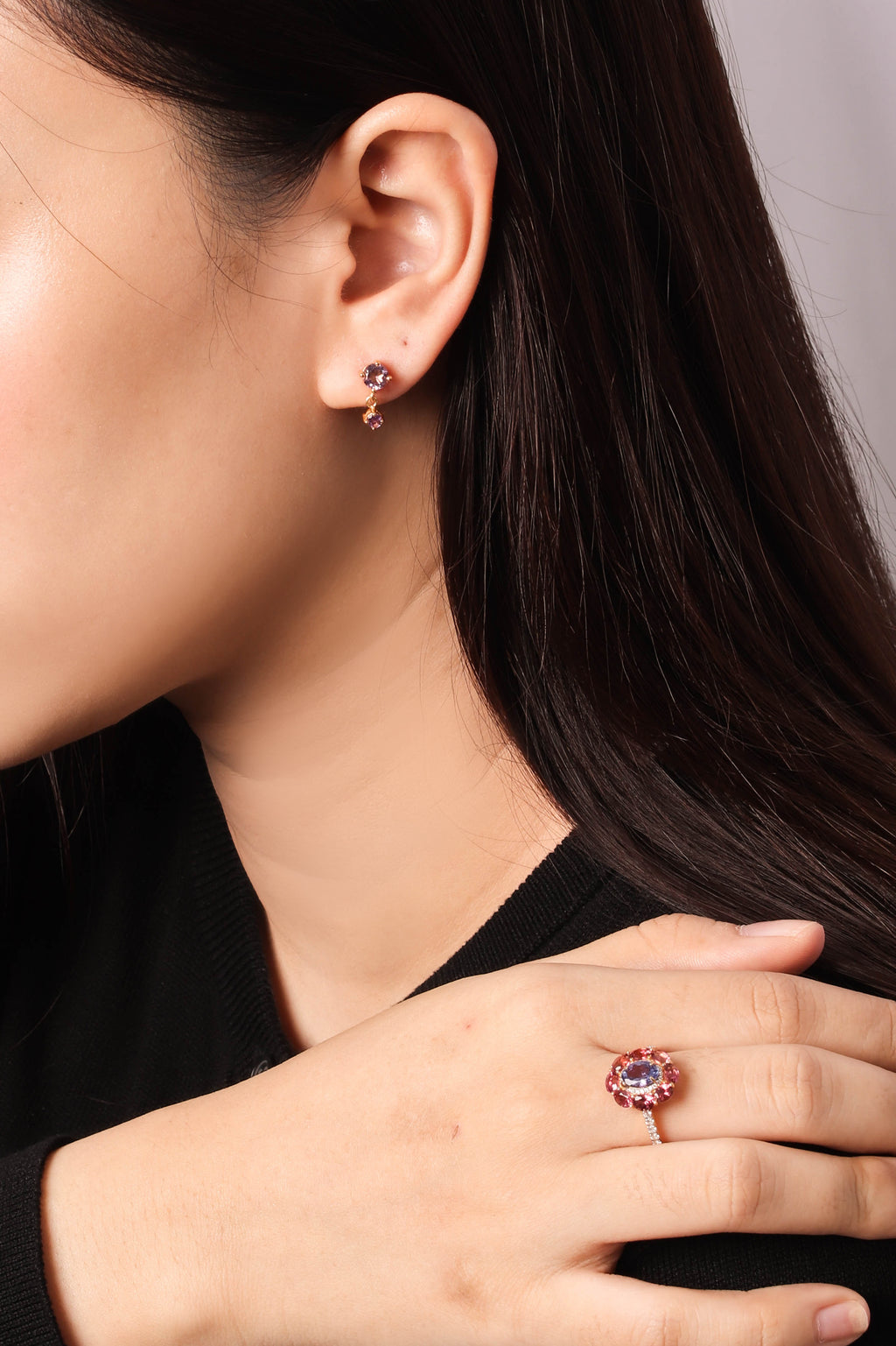 A close-up lifestyle shot of a woman wearing a rose gold ring with a round pink gemstone and matching rose gold stud earrings.