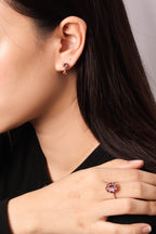 A close-up lifestyle shot of a woman wearing a rose gold ring with a round pink gemstone and matching rose gold stud earrings.