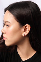 A close-up side profile of a woman with dark hair wearing a small gold hoop earring with a dark gemstone on her earlobe.