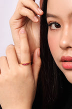 A close-up portrait of a woman wearing a delicate rose gold necklace with a snowflake pendant and a matching ring on her finger, set against a clean light gray background.