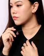 A close-up lifestyle shot of a woman wearing a delicate gold chain necklace with a small round pendant featuring a pink and green floral design. 