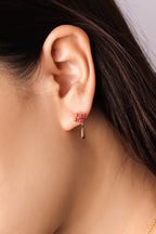 A close-up of a model's ear wearing a delicate gold dangle earring with a small cluster of pink gemstones at the top.