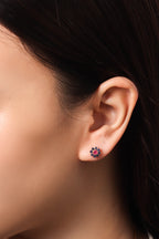 A close-up of a person's ear wearing a small flower-shaped stud earring with dark blue and pink stones.