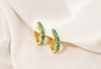 Gold hoop earrings with green gemstones on a white fabric background