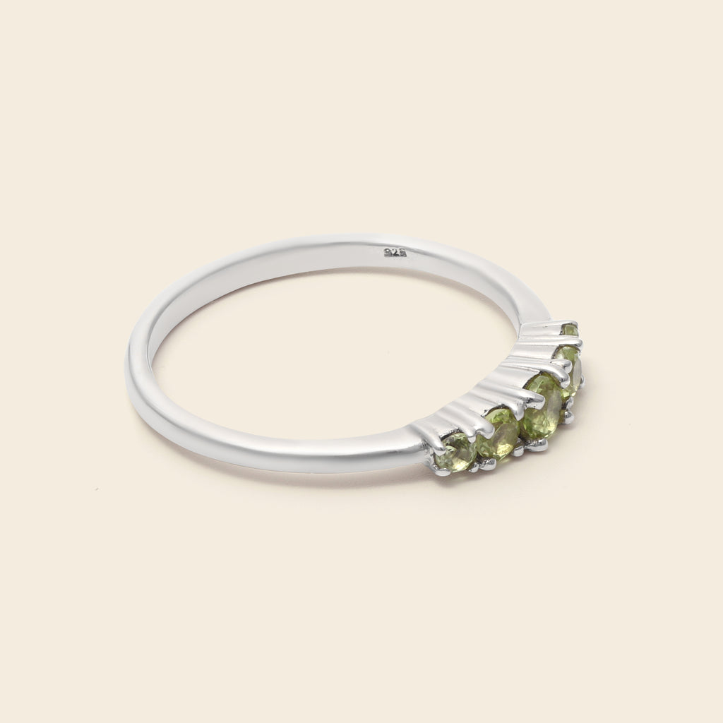 A silver ring featuring a row of small green gemstones on a light beige background.