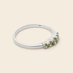 A silver ring featuring a row of small green gemstones on a light beige background.