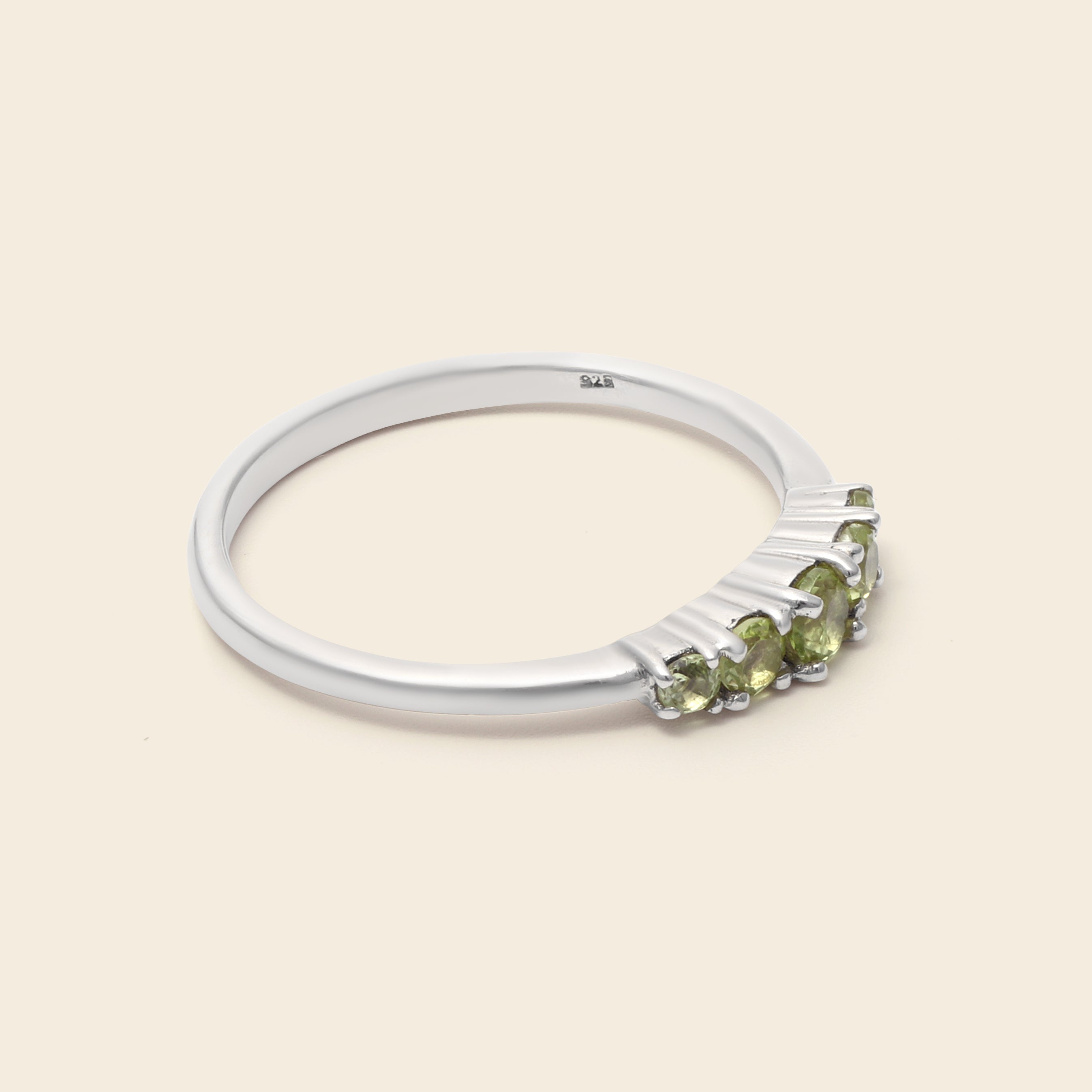 A silver ring featuring a row of small green gemstones on a light beige background.