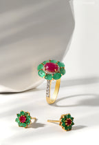 Gold ring and earrings with red and green gemstones on a white background