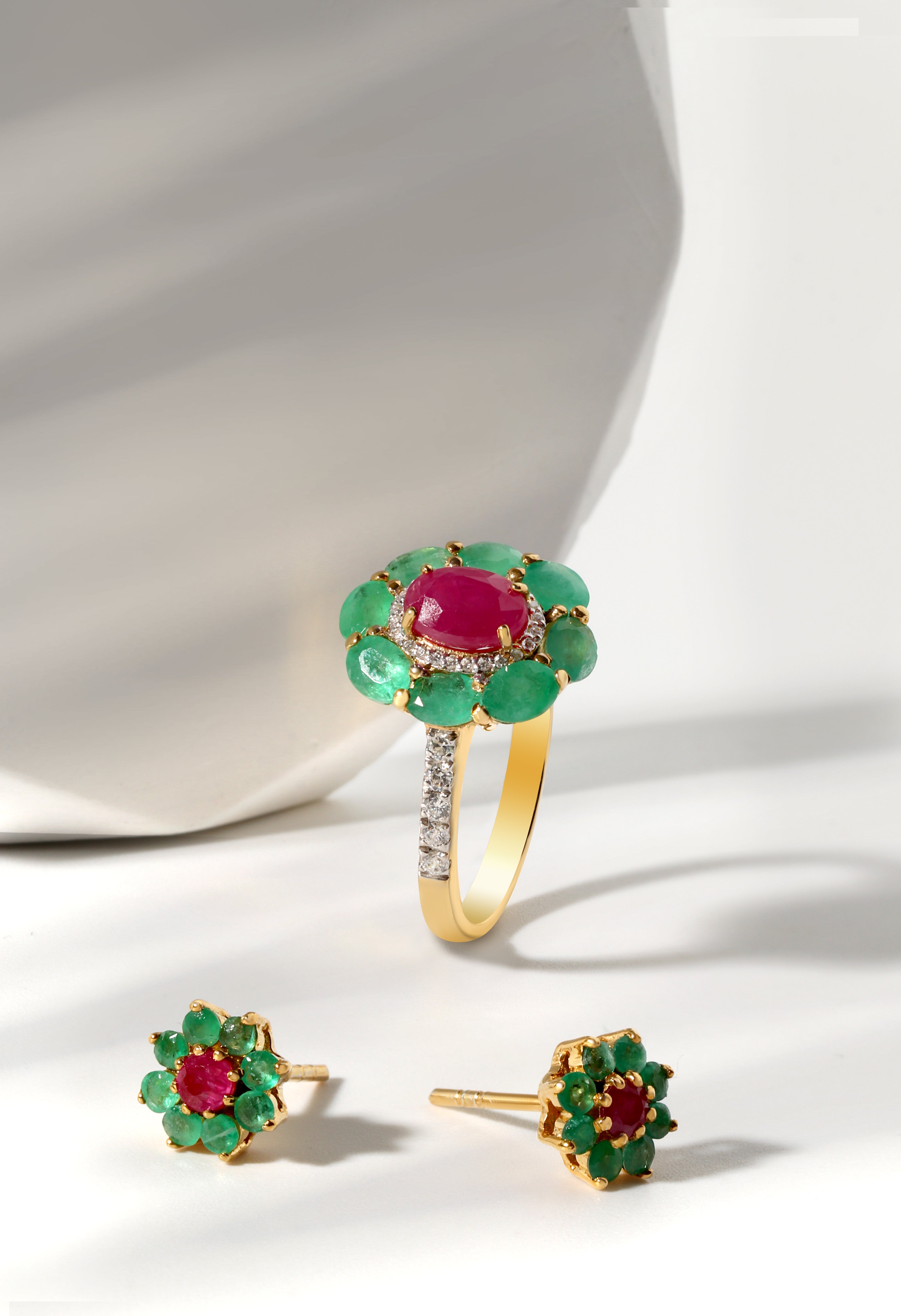 Gold ring and earrings with red and green gemstones on a white background